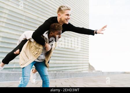 Da sotto di allegro giovane ragazzo nero che dà cavalcata piggyback ad un amico gioioso mentre si passa il tempo insieme nel parco cittadino Foto Stock