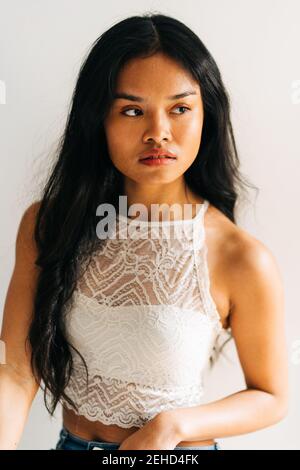Brunette capelli lunghi Asian Woman indossando una parte superiore bianca e guardando lontano Foto Stock