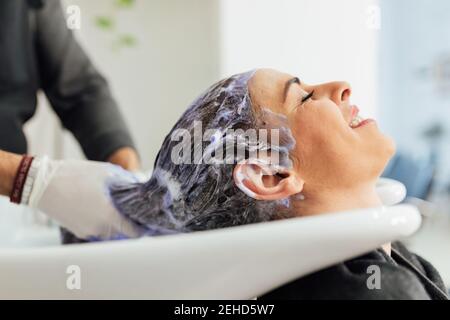 Crop maschio parrucchiere in grembiule lavaggio capelli di cliente femminile in lavello dopo il taglio e la tintura nel salone di bellezza moderno Foto Stock