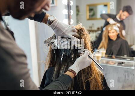 Vista laterale dei trefoli di combinatori etnici maschili focalizzati di cliente femminile irriconoscibile prima della tintura nella tecnica di balayage Foto Stock