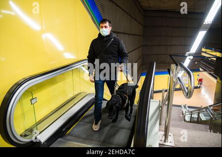 Uomo cieco che cammina sulla scala mobile con cane guida Foto Stock