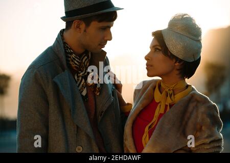 Crop uomo in abbigliamento alla moda vicino partner femminile in vintage cappello che si guarda l'un l'altro di sera Foto Stock