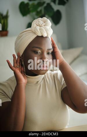 Splendida giovane donna africana modello in stile tradizionale turbante seduta davanti allo specchio a casa Foto Stock