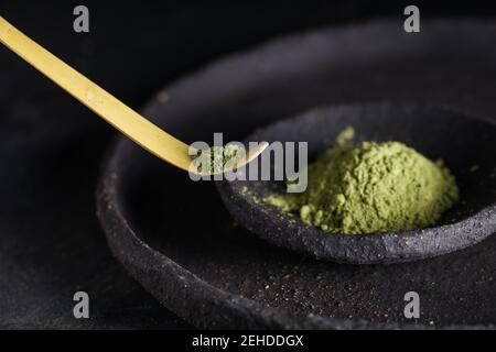 Cucchiaio con foglie di tè matcha essiccate su stoviglie nere per cerimonia orientale tradizionale Foto Stock