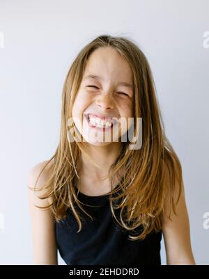 Allegra ragazza dai capelli giusti in camicia con gli occhi chiusi ridendo felicemente su sfondo bianco Foto Stock