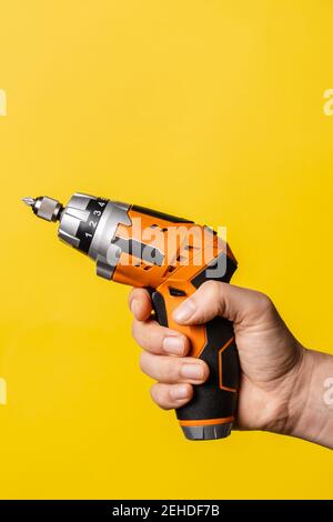 Mano di un uomo sconosciuto che tiene un cacciavite elettrico - presa maschio attrezzatura da lavoro su sfondo giallo brillante - ristrutturazione riparazione strumenti per apparecchiature elettriche Foto Stock