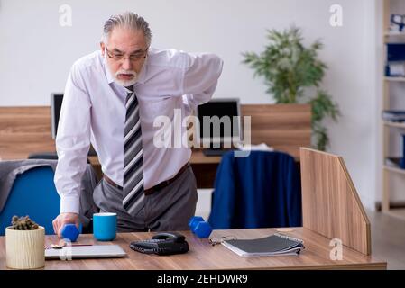 Anziano dipendente che soffre di radicolite sul posto di lavoro Foto Stock
