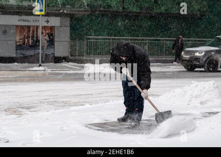 Mosca. Russia. 12 febbraio 2021. Un operatore di servizi che indossa una maschera protettiva, indossa una pala per la neve su una strada cittadina durante una nevicata su un Foto Stock