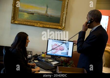 11 dicembre 2014 'il presidente parla al telefono con il vice consulente nazionale per la sicurezza ben Rhodes, mentre Ferial Govashiri mostra una fotografia sul suo computer del figlio neonato di ben'. Foto Stock