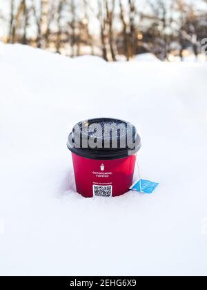 Mosca. Russia. 19 febbraio 2021. Primo piano della tazza di carta rossa nella neve bianca. Sul coperchio della tazza sono presenti fiocchi di neve. All'interno della tazza è disponibile un contenitore monouso Foto Stock