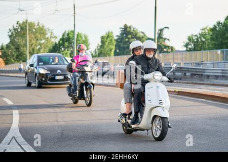Coppia anziana in moto nel traffico cittadino di strada. Motociclisti che guidano moto e automobili sulla strada. Milano - 26 maggio 2020 Foto Stock