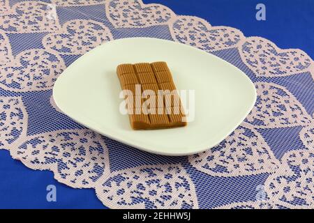 Tofee le piazze caramelle su un piatto bianco con cuore rosa corridore tavolo su tovaglia blu Foto Stock