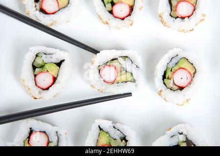 Primo piano Vista dall'alto del sushi dei California Rolls su un piatto di porcellana quadrato grande con bastoncini neri. Foto Stock
