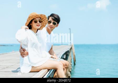 Luna di miele romantoc coppia abbracciare e seduta su legno ponte e gode la loro vacanza tropicale. Concetto di amore. Foto Stock