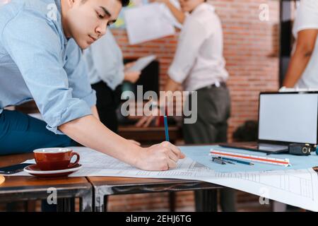 gli ingegneri che tengono una penna che punta a un edificio e disegnano un piano di costruzione di esborsi come guida per i costruttori con i dettagli. Progettazione e scrittura di ingegneri b Foto Stock