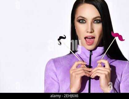 Ritratto di bruna donna eccitato in viola maniche lunghe tenuta baffi decorativi rosa e nero nelle mani Foto Stock