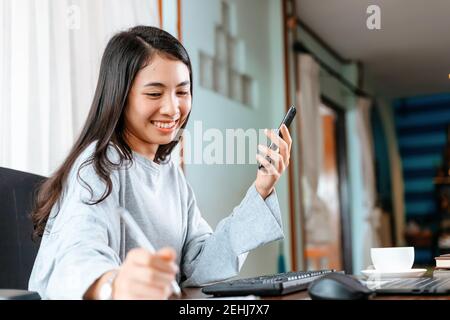 donna che usa il telefono cellulare mentre lavora a casa. Foto Stock