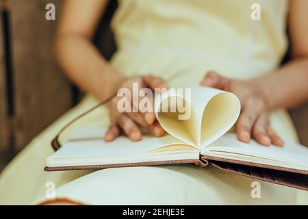 le mani fanno un libro carta forma cuore. Concetto di amore. Foto Stock