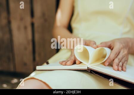 le mani fanno un libro carta forma cuore. Concetto di amore. Foto Stock