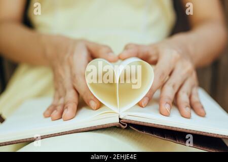 le mani fanno un libro carta forma cuore. Concetto di amore. Foto Stock