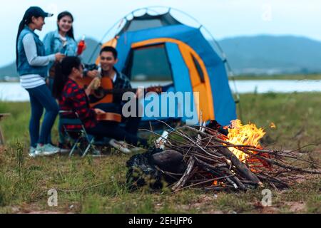 Fuoco al campo e gruppo di amici bere birra insieme. camp e concetto di viaggio. Foto Stock