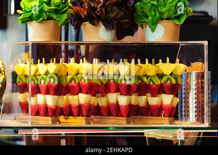 Pezzi di frutta esotica su bastoni, fragole, pere, kiwi e ananas. Visualizzazione precisa in una custodia in vetro trasparente. Foto Stock