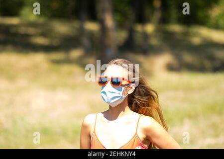 Ragazza con occhiali da sole in pixel rosso che indossa una maschera di precezione in una giornata di sole in tempi pandemici. Foto Stock