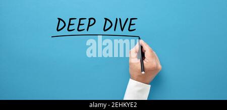 Mano dell'uomo d'affari che scrive la parola d'ordine immersione profonda su sfondo blu. Foto Stock