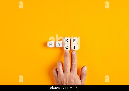 Mano maschile spingendo i cubi di legno e trasformando la parola falso a fatto su sfondo giallo. Concetto falso contro fatto. Foto Stock