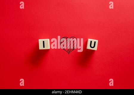 Ti amo parola scritta su cubi di legno con una forma a cuore disegnata a mano su sfondo rosso. Concetto di giorno di San Valentino. Foto Stock