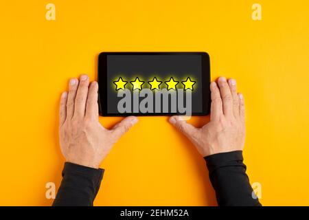 Mano maschile che tiene un tablet digitale con cinque stelle sullo schermo. Servizio clienti o concetto di valutazione del prodotto. Foto Stock