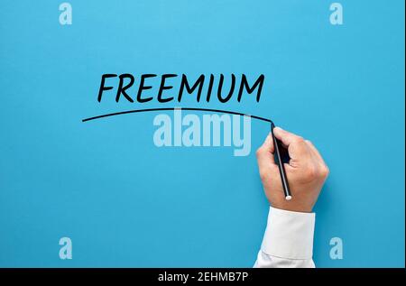 Mano di uomo d'affari che scrive la parola freemium su sfondo blu. Strategia di marketing di utilizzare contenuti gratuiti per attirare nuovi clienti nel business. Foto Stock