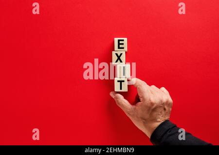 Mano maschile disposizione dei blocchi di legno con la parola uscita su sfondo rosso con spazio di copia. Decisione di uscire o uscire dalla strategia nel concetto di business. Foto Stock