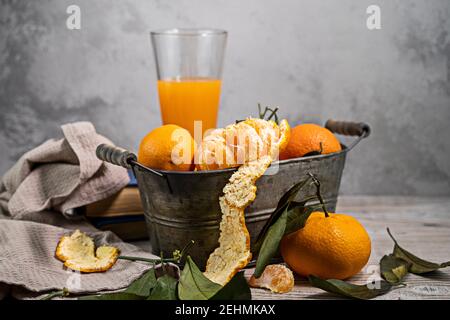 Diversi tangerini maturi con foglie in un contenitore giacciono su un tavolo bianco su uno sfondo chiaro. Copyspace in stile rustico. Foto Stock