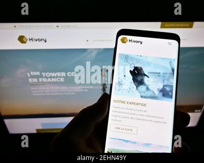 Persona che detiene il telefono cellulare con il sito web e il logo della società francese di telecomunicazioni Hivory di fronte allo schermo. Mettere a fuoco in alto a sinistra del display del telefono. Foto Stock
