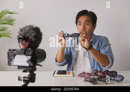 Asian Vlogger o Blogger in Jean Shirts mostra occhiali di moda nero mentre la registrazione video. Freelance Online Live Streaming con il cliente tramite Social Me Foto Stock