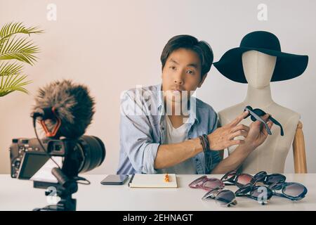 Asian Vlogger o Blogger in camicie Jean con occhiali di moda Mannequins Point e video di registrazione. Freelance Online Live Streaming con il cliente via Foto Stock