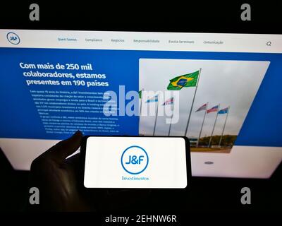 Persona che detiene smartphone con logo della società di investimento brasiliana J e F Investimentos S.A. sullo schermo di fronte al sito web. Mettere a fuoco il display del telefono. Foto Stock