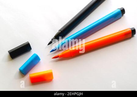 Tre nuovi pennarello multicolore su sfondo bianco. Penne in feltro nere, arancioni e blu per la verniciatura senza tappi. Primo piano, messa a fuoco selettiva Foto Stock