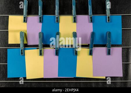 Le note appiccicose di carta appese ai clothespins. Set di adesivi quadrati bianchi multicolore su sfondo nero. Nessuna gente. Foto Stock