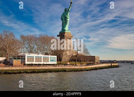 La Statua della libertà a New York City USA luce del giorno Vista dal retro di Liberty Island con le nuvole il cielo sullo sfondo Foto Stock