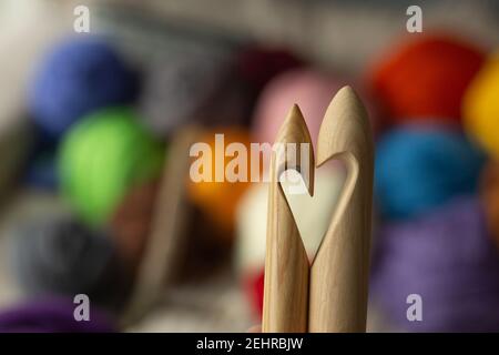 Due aghi in legno da maglieria, su uno sfondo di matasse colorate di merino, a forma di cuore Foto Stock