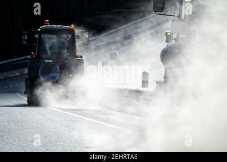 Spazzare la superstrada dopo l'inverno, servizio su strada. Un trattore speciale (macchina spazzatrice stradale) con una scopa cilindrica spazza la strada, auto sollevata qu Foto Stock