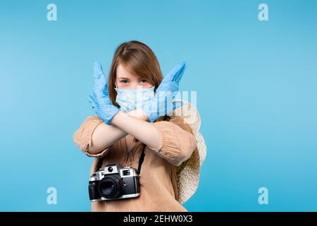 Una ragazza in una maschera medica con una macchina fotografica sul collo, che attraversa le braccia, guarda la macchina fotografica. Stop. La fine della diffusione del virus. Foto Stock
