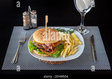 Pasto di hamburger di manzo con patatine sul lato, su un piatto bianco e uno sfondo nero. Fast food di qualità. Foto Stock