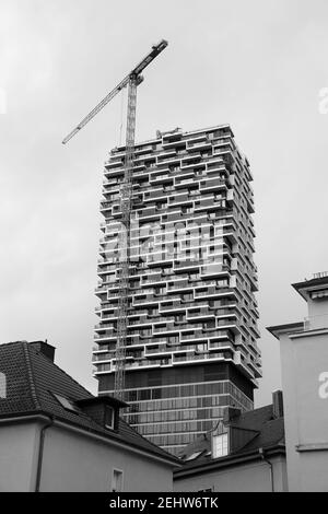 Immagine verticale in scala di grigi di una gru a torre e di una nuova edificio residenziale contro un cielo nuvoloso Foto Stock