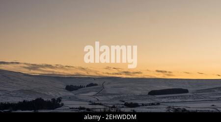 Nel tardo pomeriggio bagliore nel cielo sul paesaggio innevato del North Pennine (Weardale, County Durham) Foto Stock