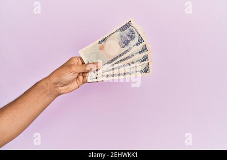 Mano ispanica che tiene 5000 yen giapponesi su sfondo rosa isolato. Foto Stock