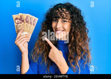 Giovane ragazza ispanica che tiene 5000 banconote forint ungheresi sorridenti felici puntare con la mano e il dito Foto Stock