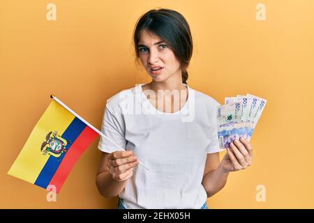 Giovane caucasica che detiene la bandiera della colombia e pesos colombiani banconote indecchiare e confuse espressione. Concetto di dubbio. Foto Stock